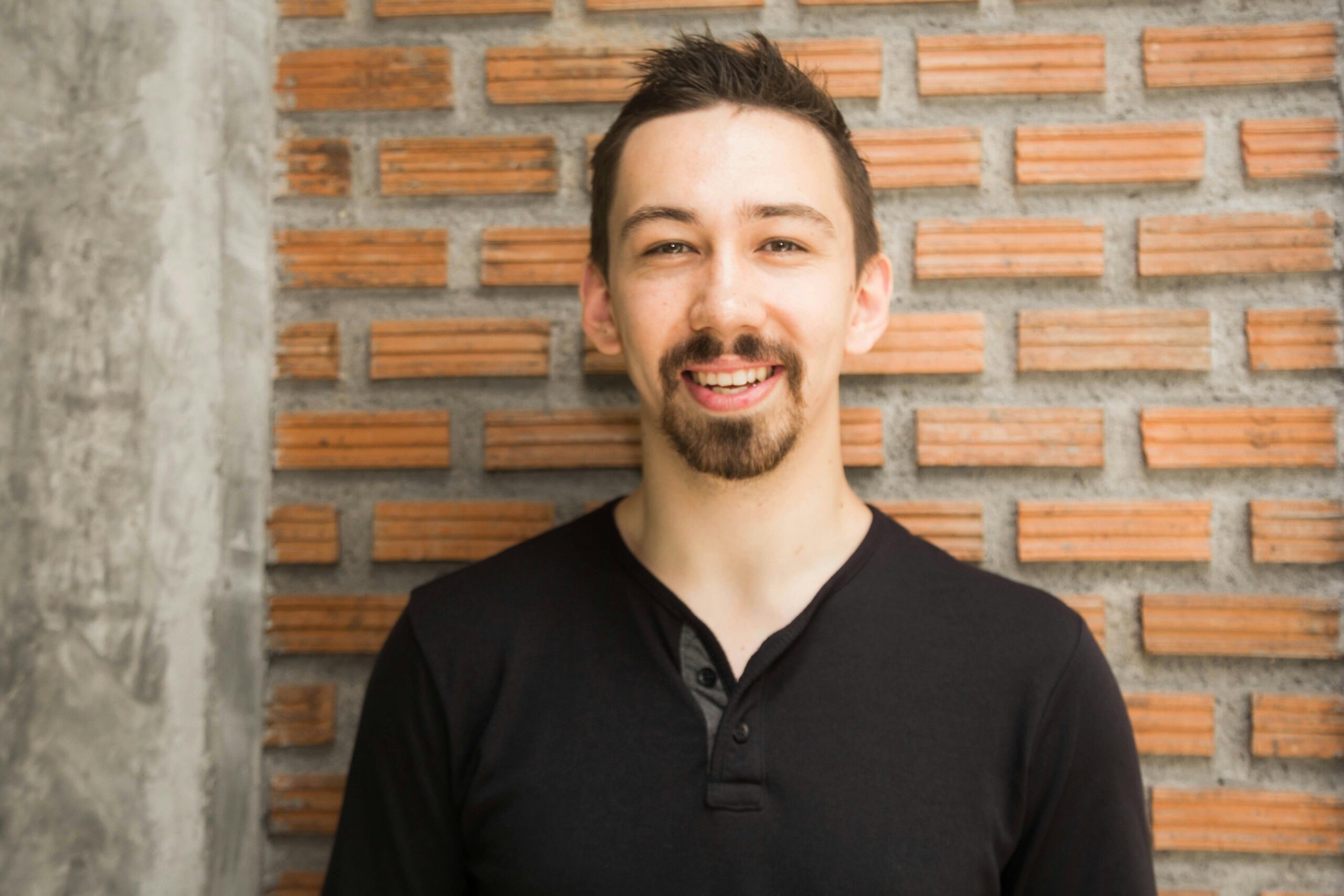 Portrait of a smiling man with a beard standing against a brick wall